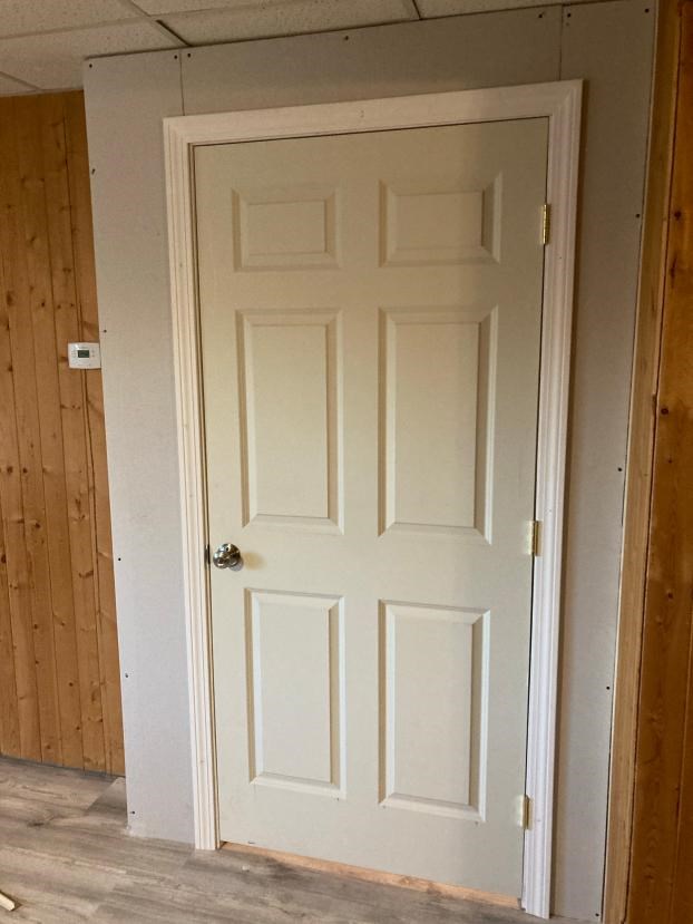 White door with trim set into drywall, wood panel wall adjacent.